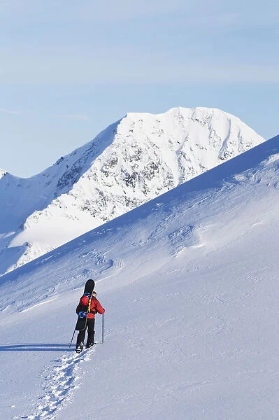 Backcountry Snowboarder Hiking Through The Snow Towards A Mountain Peak, Eagle Glacier, Chugach Mountains, Southcentral, Alaska