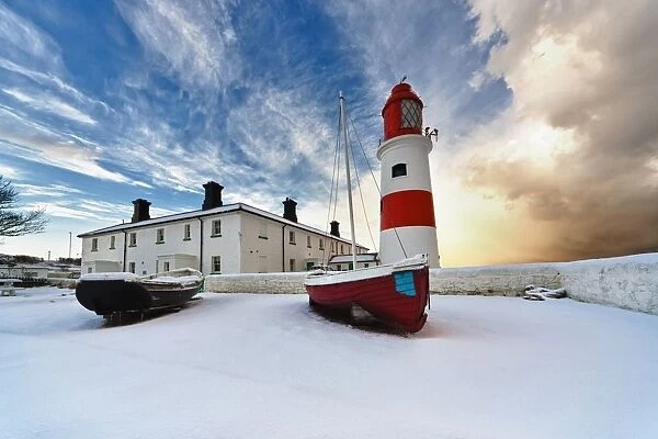 Boats Sitting On A Frozen Surface With A Lighthouse And Building In The Background; South Shields, Tyne And Wear, England