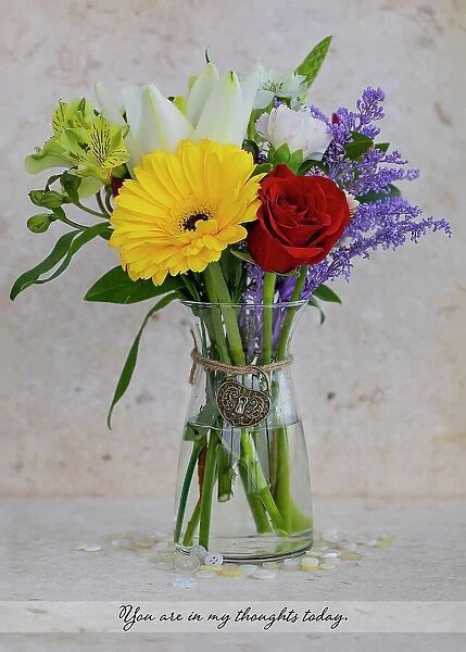 Colorful bouquet in glass vase with a thoughtful message in text and a heart-shaped charm, studio