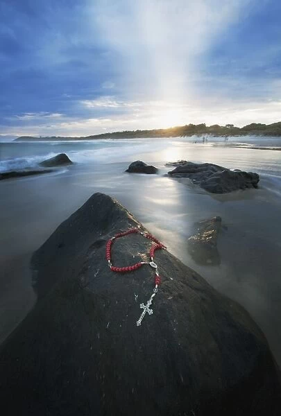 A Cross And Rosary Beads Laying On A Rock At Flat Rock; Bellina, New South Wales, Australia