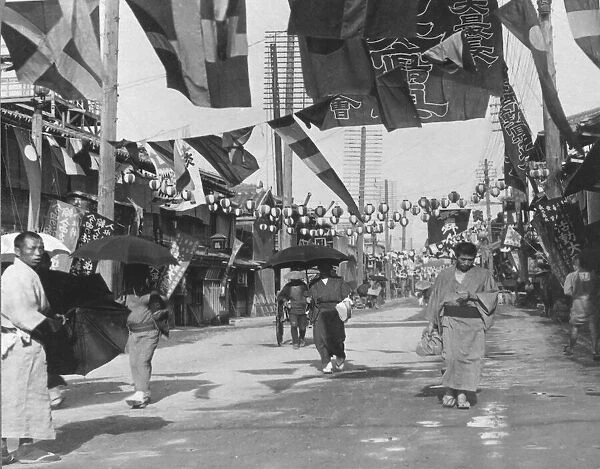 Historic image in black and white of people walking down the street in Dotombori, Osaka, Japan, the theatre district and traditional street scene with lanterns, flags, a rickshaw and people carrying umbrellas; Osaka, Kansai, Japan