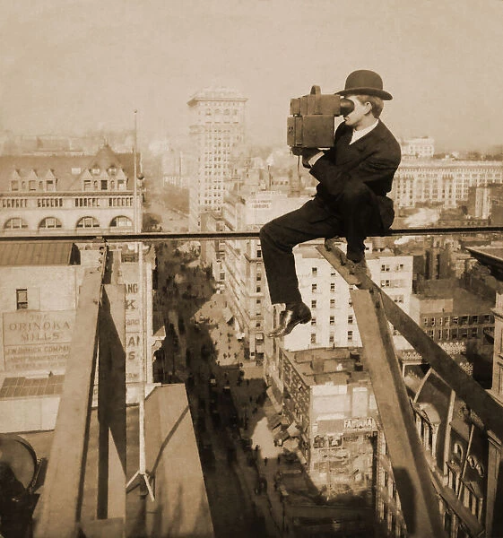 Historic image in sepia of a photographer sitting on a slender girder above fifth avenue in New York City with a stereocamera, circa 1905; New York City, New York, United States of America