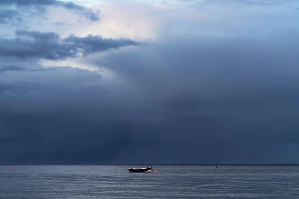 Lone rowboat moored under dark stormy sky