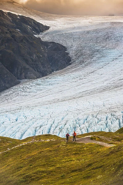 A Man And Woman Hiking Down The Harding Icefield Trail With Exit Glacier In The Background, Kenai Fjords National Park, Kenai Penninsula, Southcentral Alaska