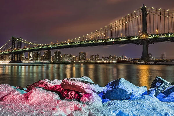 Manhattan Bridge By Snow-Covered Rocks At Sunset, Brooklyn Bridge Park; Brooklyn, New York, United States Of America
