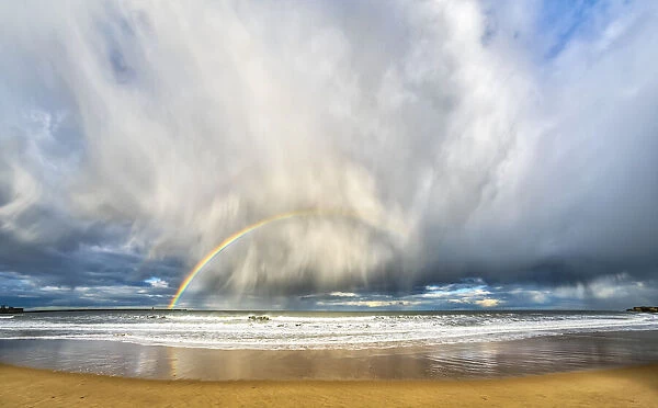 Rainbow through storm clouds viewed from a beach