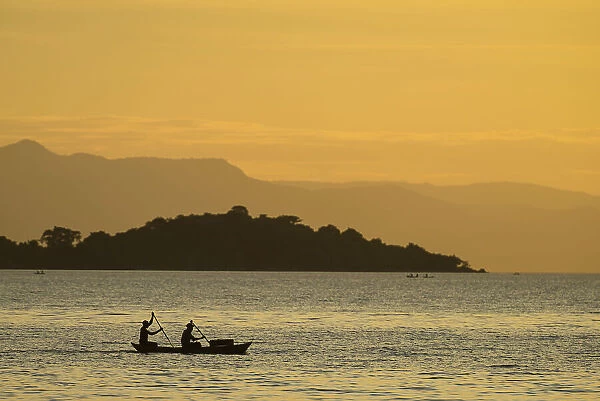 Silhouette Of Fishermen In Dugout Canoe Leaving Cape Maclear In The Evening, Lake Malawi; Malawi