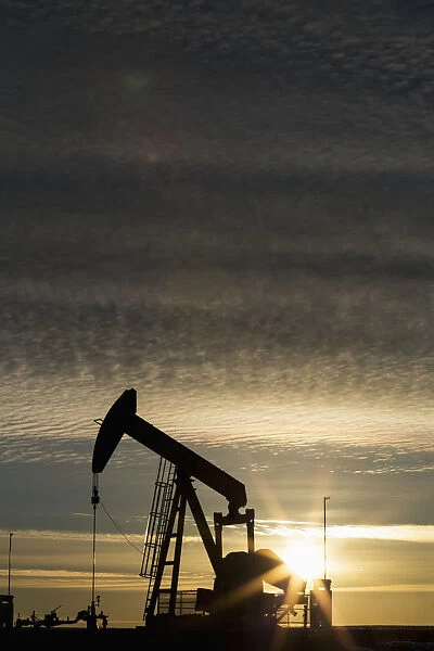 Silhouette Of Pump Jack At Sunrise With Sun Burst And Colourful Clouds In The Sky; Alberta, Canada