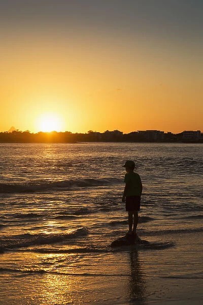 Silhouette Of A Young Boy Standing At The Waters Edge At Sunset; Caloundra, Queensland, Australia