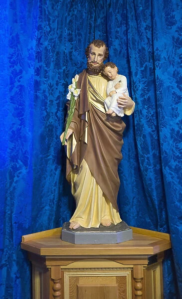 Statue Of Jesus Holding A Child In Front Of A Blue Curtain; Northumberland, England