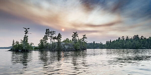 Sun glowing in clouds over a lake and forest at sunset, Lake of the Woods, Ontario; Kenora, Ontario, Canada