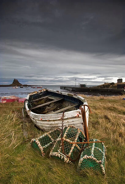 A Weathered Boat And Fishing Equipment Sitting On The Shore With Lindisfarne Castle In The Distance; Lindisfarne, Northumberland, England