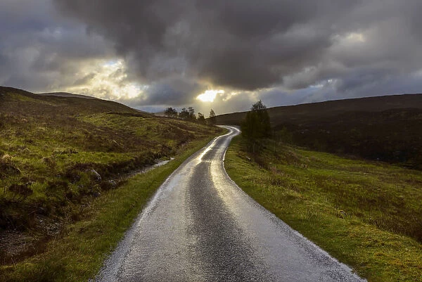 Winding road in the highlands with sun shining through the dark clouds at Glen Coe in Scotland, United Kingdom