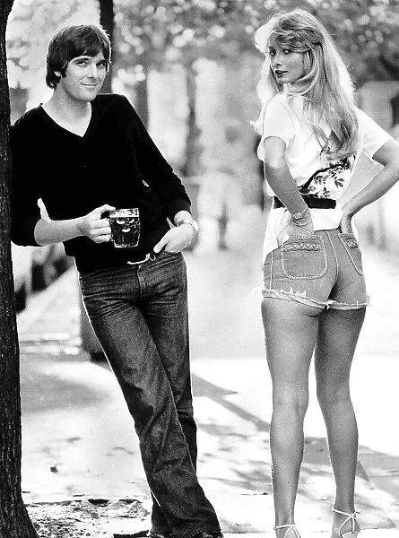 Actor Steve Alder holding a pint of beer as he poses with a model wearing denim hot pants