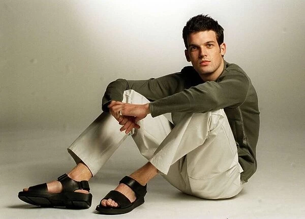 Adam Sinclair actor in studio January 1999 wearing green jumper cream trousers sandals