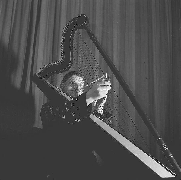 Benny Hill displaying a rather novel way of enjoying a cigarette whilst playing the harp
