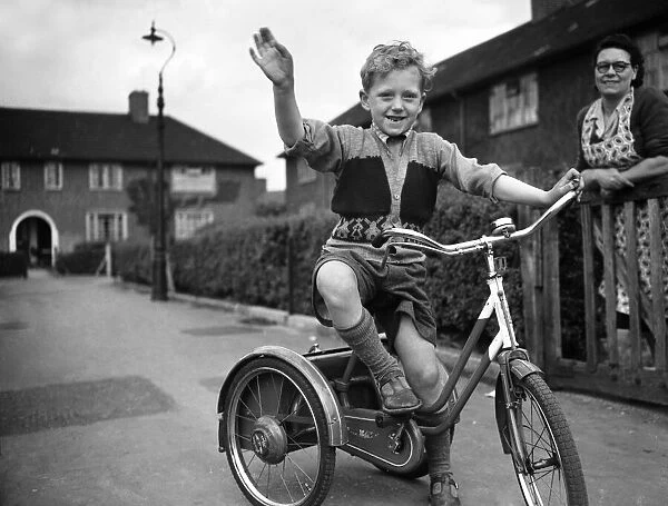 A boy plays on his tricycle on a council estate as his mother looks on 1955