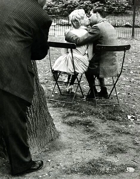 A couple kissing in the park all the while being watched by a dirty old man