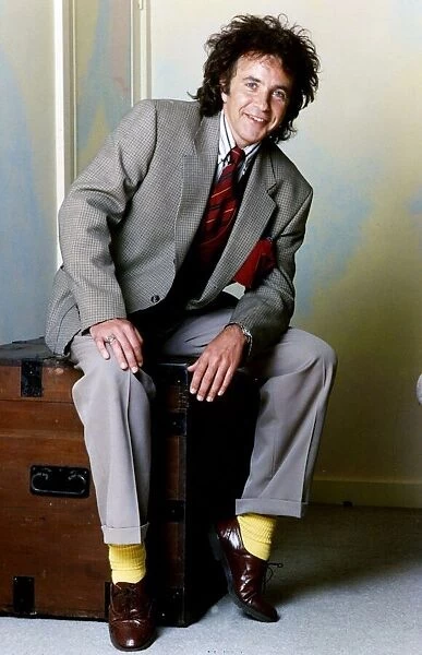 David Essex Singer sitting on a blanket box wearing a suit and yellow socks