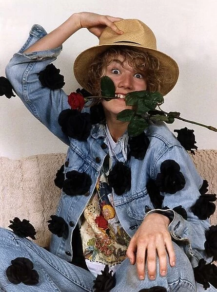 Emily Lloyd Actress sitting with hand on top of hat and with red rose in teeth