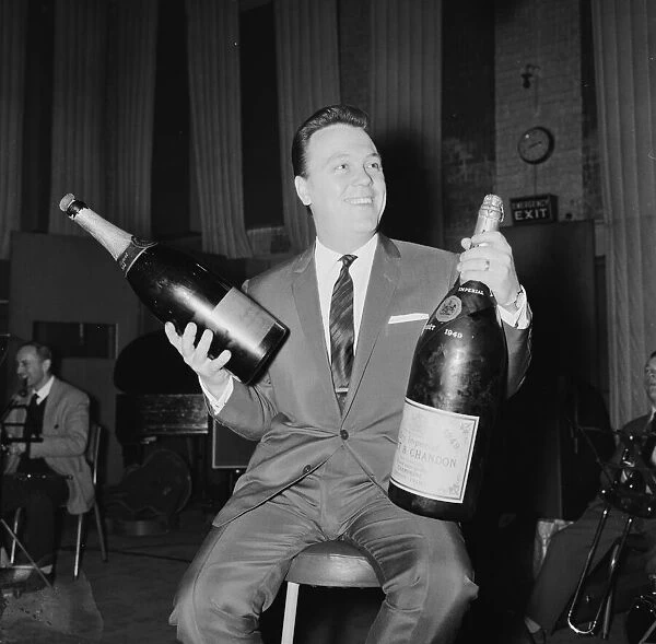 English singer Matt Monro with a giant size bottle of champagne as he works on his latest