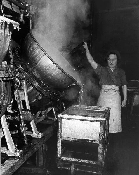 A factory worker tipping a huge cauldron of boiling jam
