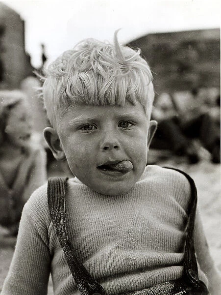 Little boy with sand all over him, tousled hair and ice cream tongue sticking out his