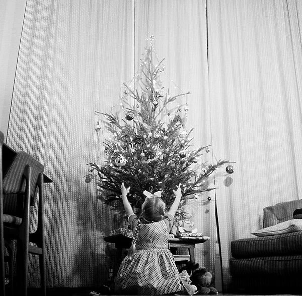 A little girl sits in front of a christmas tree. 28th December 1961