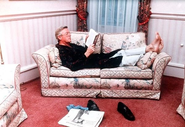 Michael Aspel TV Presenter of This is your Life lying on sofa reading book