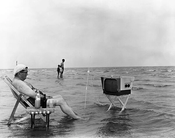 A seaside scene of a man watching television on the beach. Littlehampton, West Sussex