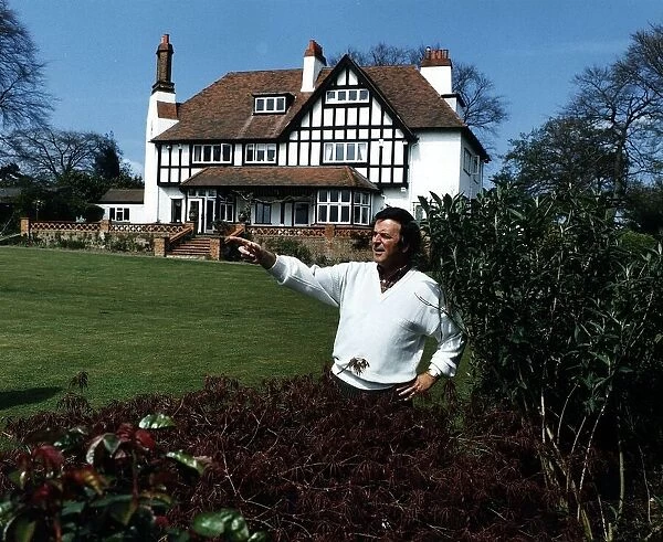 Terry Wogan Radio and TV Presenter stands and points in his garden in front of his house