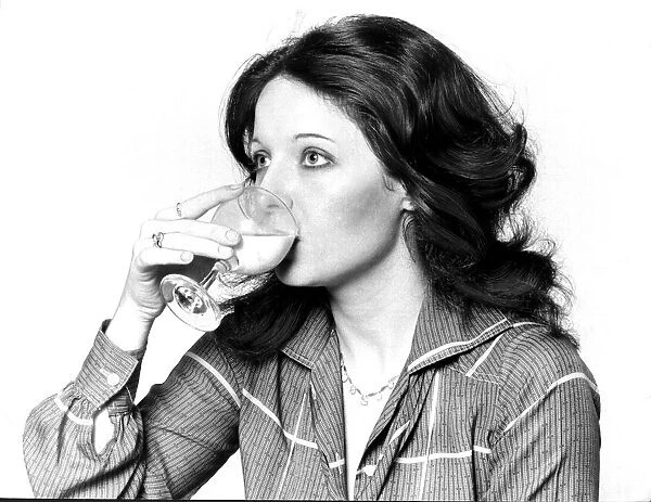 Woman drinking a cocktail from a wine glass September 1977