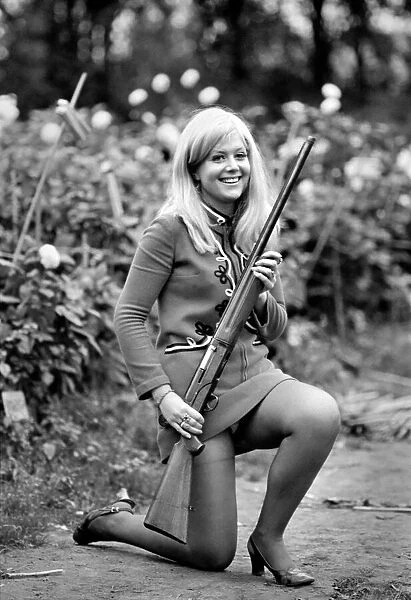 A woman posing wearing a mini dress and holding a shot gun November 1969