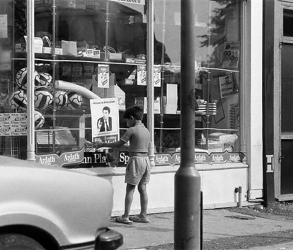 A young boy puts up a Muhammad Ali poster on a shop window in Birmingham
