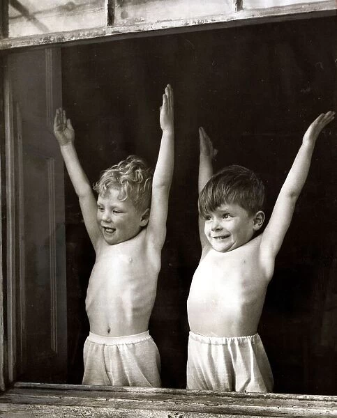 Two young boys doing stretching and breathing exercises in front of an open window at