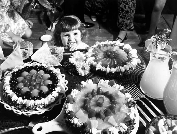 A young girl looking at a table with cakes. 1970