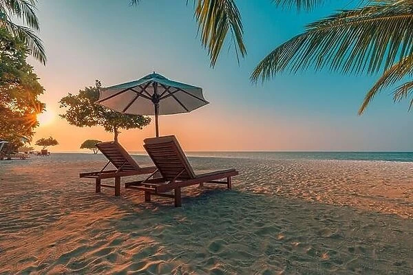 Beautiful tropical sunset scenery, two sun beds, loungers, umbrella under palm tree. White sand, sea view with horizon, colorful twilight sky calmness