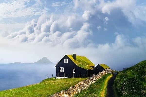 Foggy morning view of a house with typical turf-top grass roof and blue cloudy sky in the Velbastadur village on Streymoy island, Faroe islands