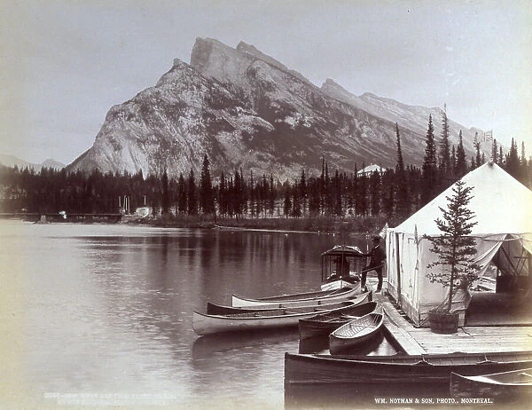 Bow river at the base of the Rocky Mountains, in Canada. In the foreground a man has stopped on a pier where a few canoes are drawn up