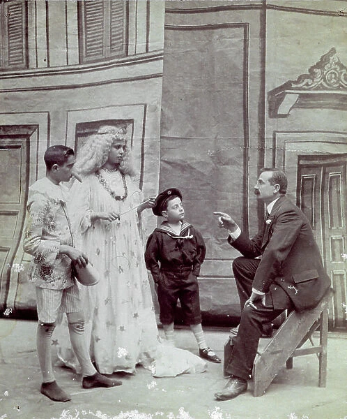 Three children in costume, respectively Pinocchio, the blue fairy and a sailorboy. The small actors are watching a man who seems to be explaining the scene to them