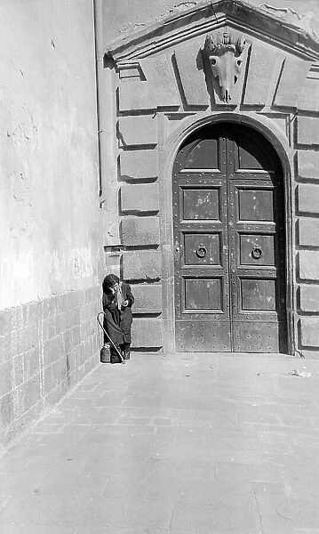 Elderly woman at the corner of the entrance portal of the convent of the church of Santo Spirito, Piazza Santo Spirito, Florence