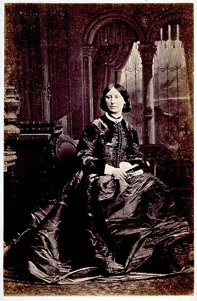 Full-length portrait of a young woman, seated. She wears luxurious daytime dress and holds a closed fan in her right hand