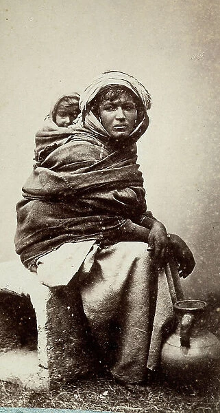 The image shows a woman sit down, carrying on her back her child. At her foot, a jug for water. The woman comes from a Bedouin tribe of northern Africa
