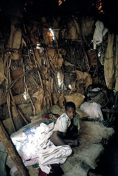 Jalalaxi: Ogaden refugee camp (war with Ethiopia). Woman intent on cooking squares of mush, inside a hut, a pallet