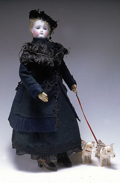 Mannequin doll with dogs on a leash made in France in the second half of the Nineteenth century. The body is dressed in a heavy walking outfit decorated with plumes, reproducing the style of the period. On her head, in bisque, an elegant hat