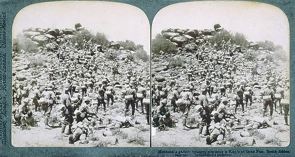 Military attack on a Boer hill in South Africa. In the foreground, various soldiers, seen from behind, as they move towards the summit of the hill. Some of them are lying on the ground, wounded