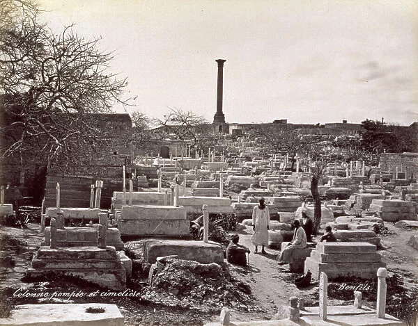 A muslim cemetery in the environs of Alexandria, in Egypt. A few men in humble ethnic dress are seated among the tombstones. In the distance, on a height, is Pompey's Pillar