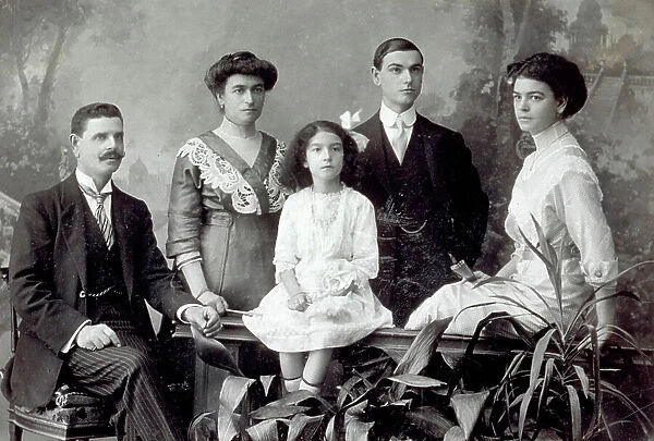 Portrait of the Giannelli family. The wife and adult son pose next to the father who is seated. In the foreground, sitting on a balustrade, the small daughter and her older sister