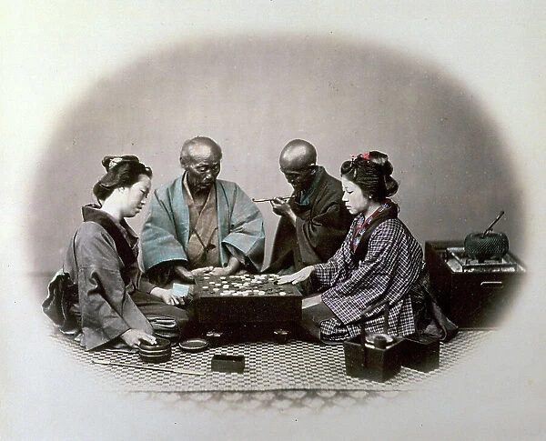 Portrait of two young japanese women playing a parlour game, by their sides two men are watching the progress of the game. They are kneeling on the ground and are wearing traditional clothes