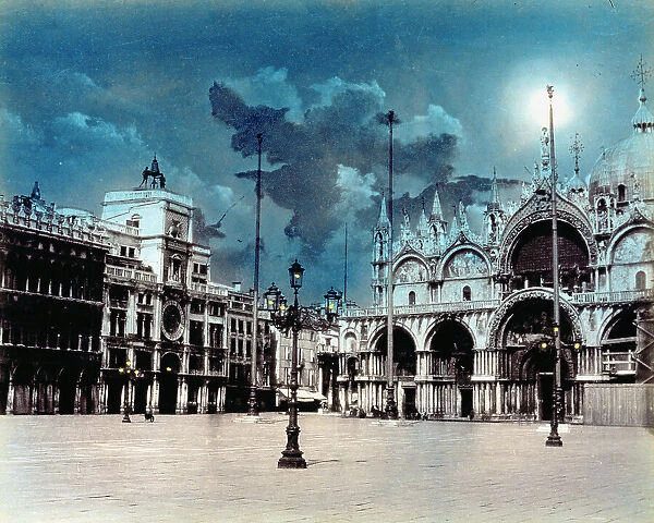 St. Mark's Square in Venice by night. The facade of the Basilica of San Marco can be seen beneath a sky full of clouds and a full moon. On the left is the Clock Tower. The square is furnished with street lamps and pennants